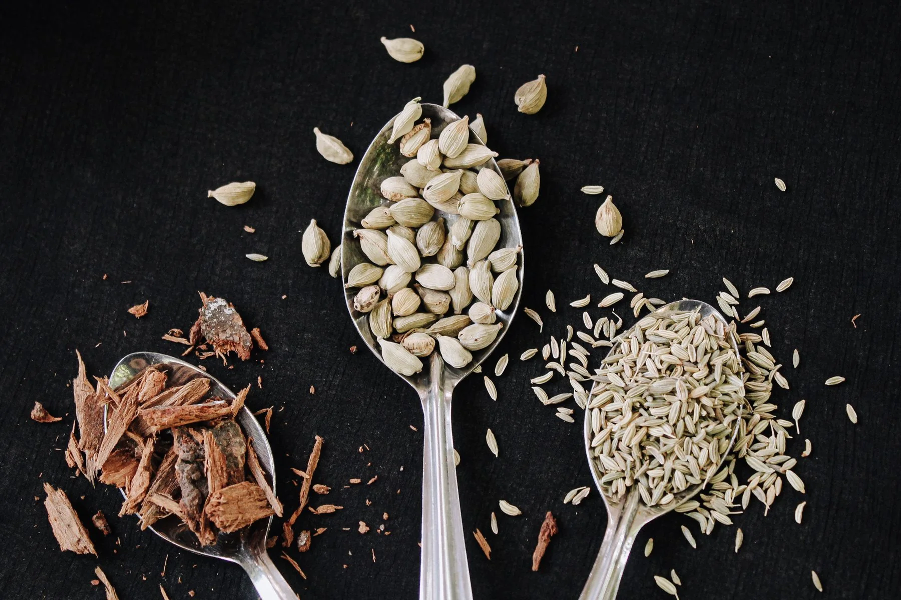 Cardamomo, canela y semillas presentadas en cucharas como ejemplo de especias ayurvédicas
