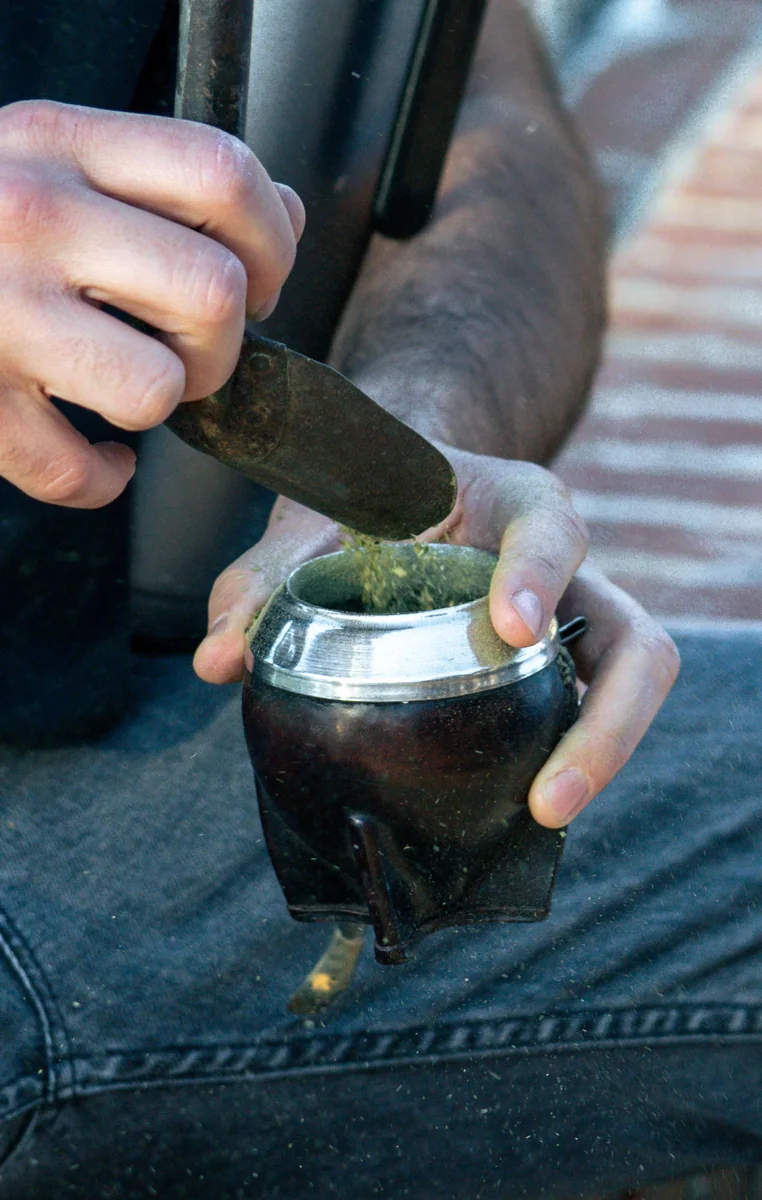Persona colocando yerba mate seca dentro de un recipiente tradicional