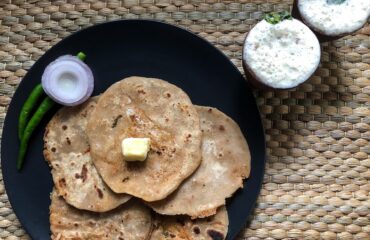 A traditional Punjabi meal consisting of aloo paratha topped with butter and served alongside a glass of fresh lassi. Photograph taken as part of Wiki Loves Food 2021.
